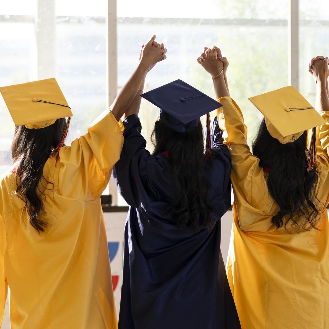 A group of graduates in blue and yellow regalia hold hands
